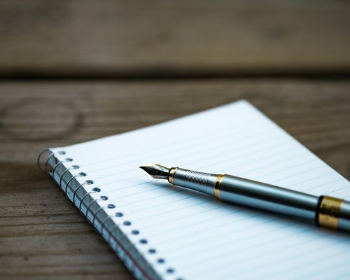 A notebook and pen resting on a wooden table next to glasses